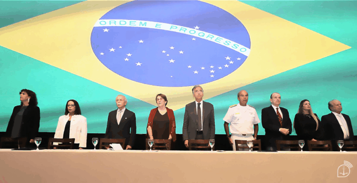 Pessoas reunidas diante da bandeira do Brasil.