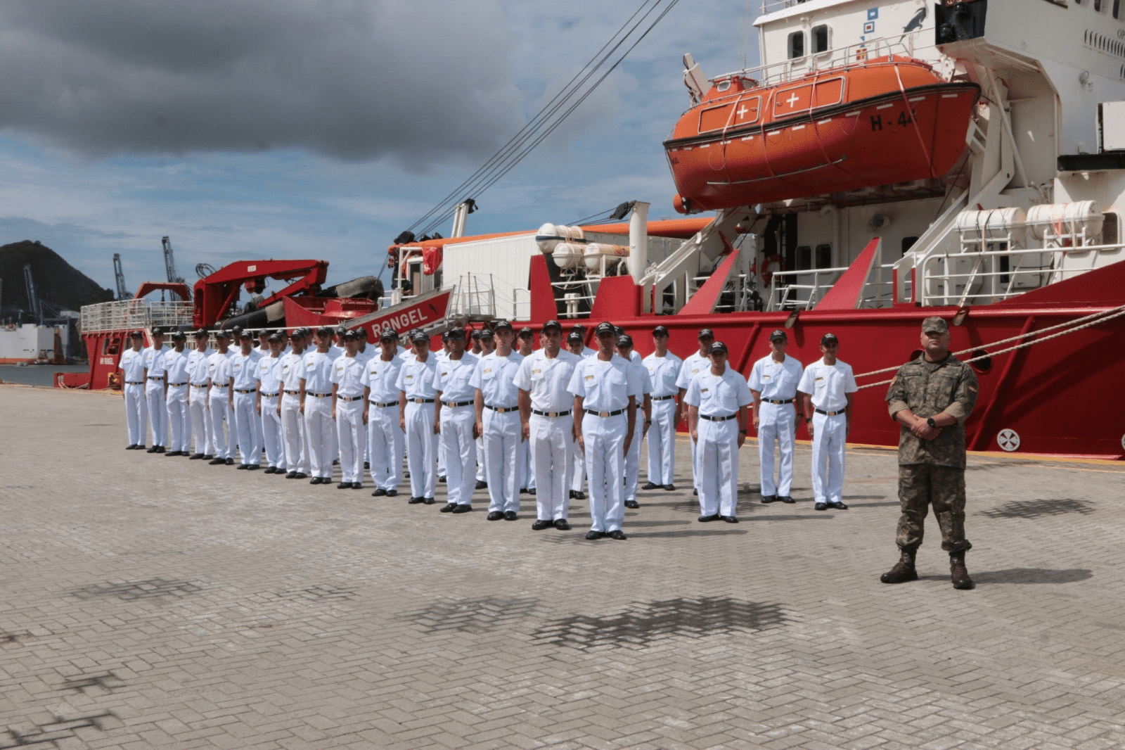 Tripulação naval alinhada em frente ao navio no porto.