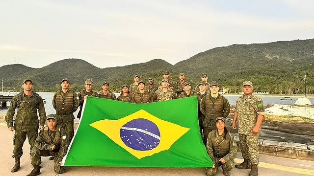 Soldados brasileiros com bandeira, montanhas ao fundo.