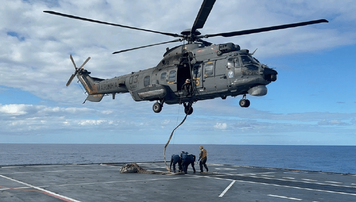 Helicóptero militar em operação sobre porta-aviões no mar.