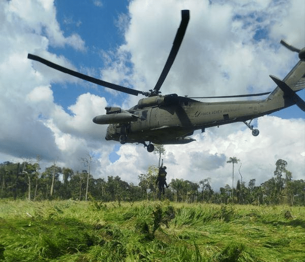 Helicóptero militar sobrevoando área verde com céu azul.