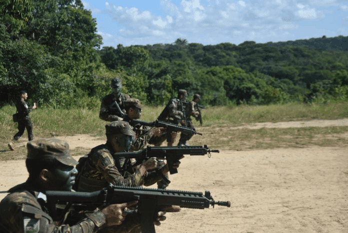 Soldados em treinamento no campo, armados e camuflados.