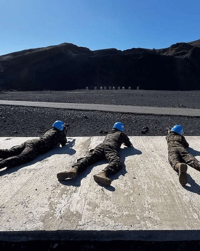 Soldados treinando tiro com capacetes azuis, chão escuro.