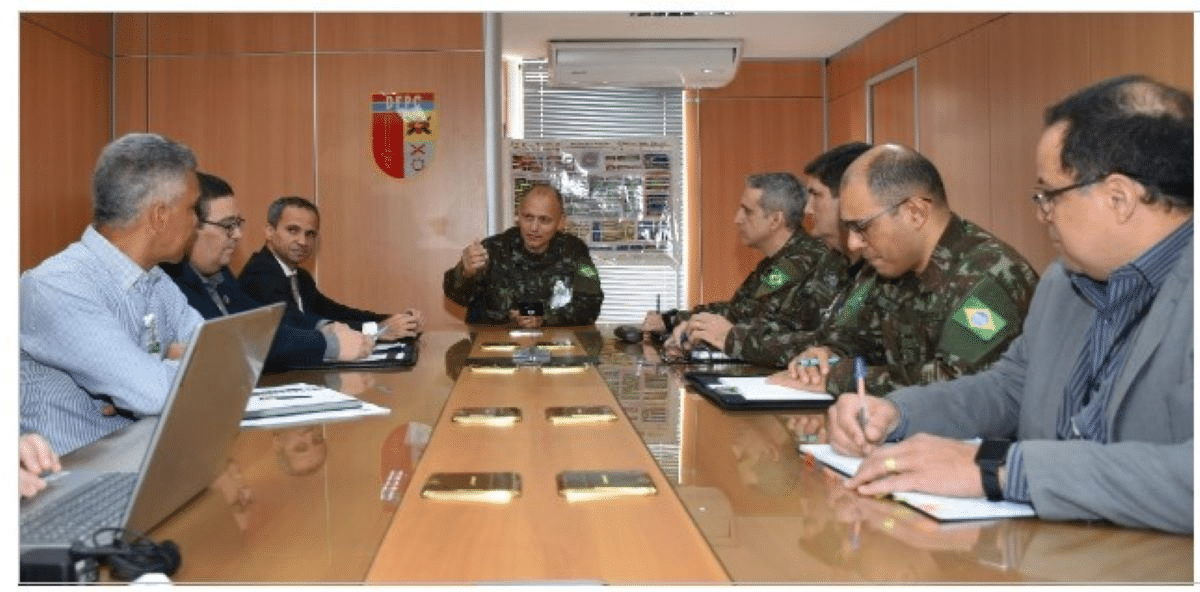 Reunião de militares e civis em mesa de conferência.