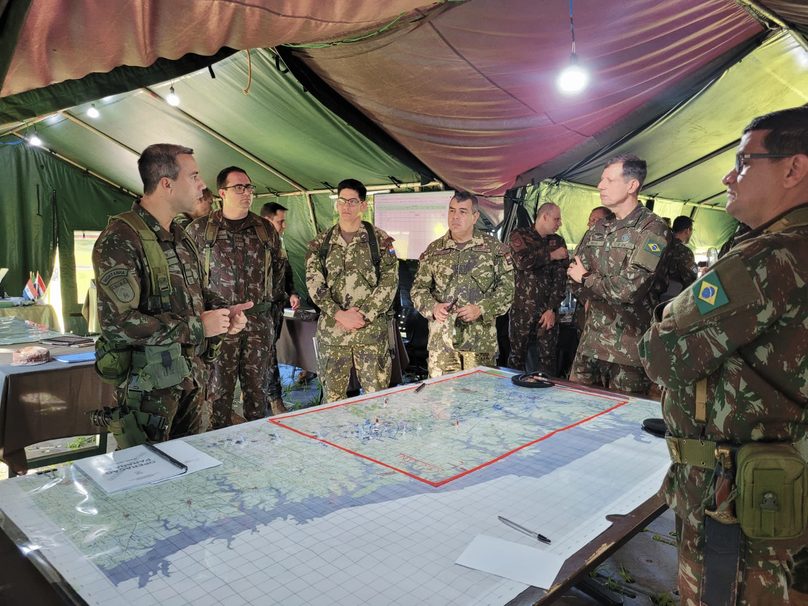 Militares discutem mapas em acampamento.