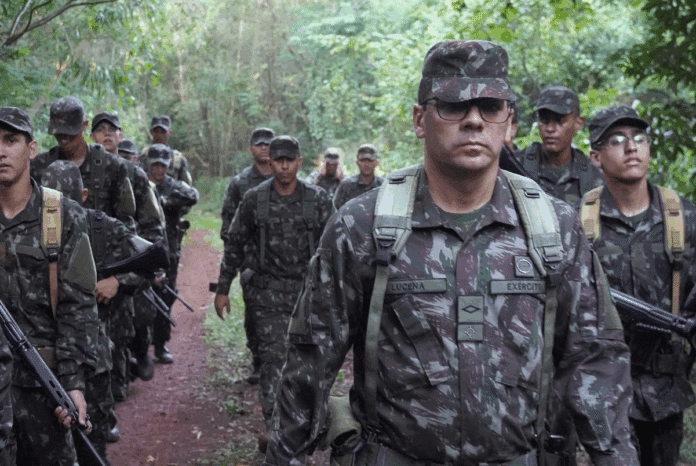 Soldados marchando em floresta tropical, uniforme camuflado.