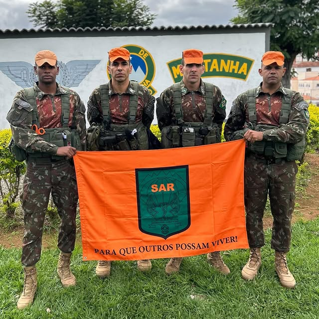 Soldados com bandeira SAR laranja em frente a mural.