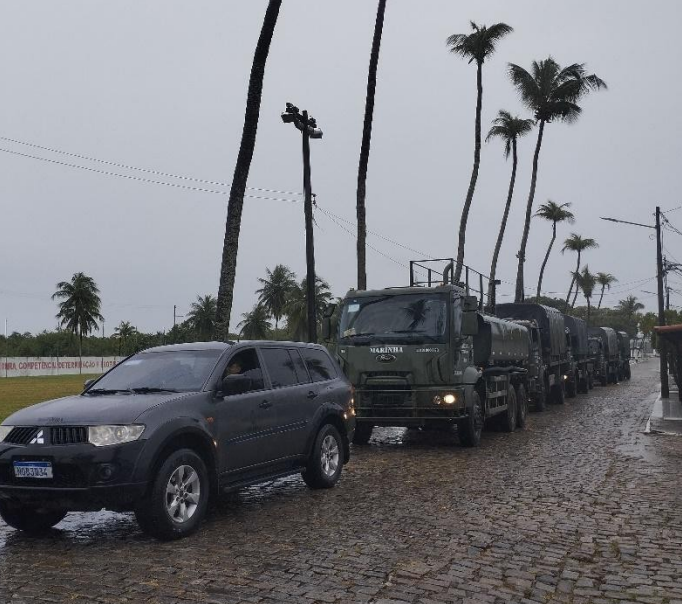 Comboio militar em rua com palmeiras ao fundo.