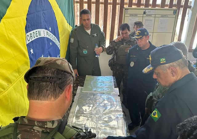 Militares discutem estratégia em frente a bandeira do Brasil.