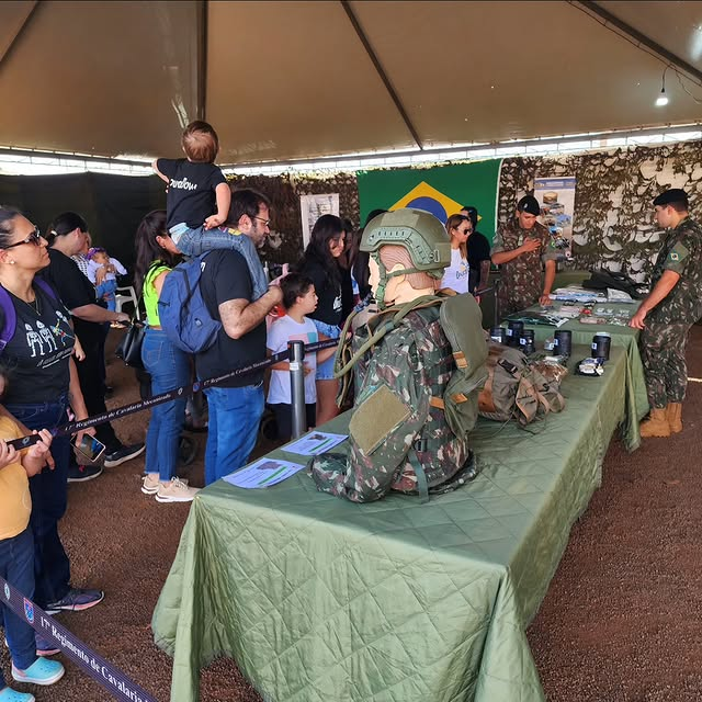 Visitantes em exposição militar com uniforme camuflado.