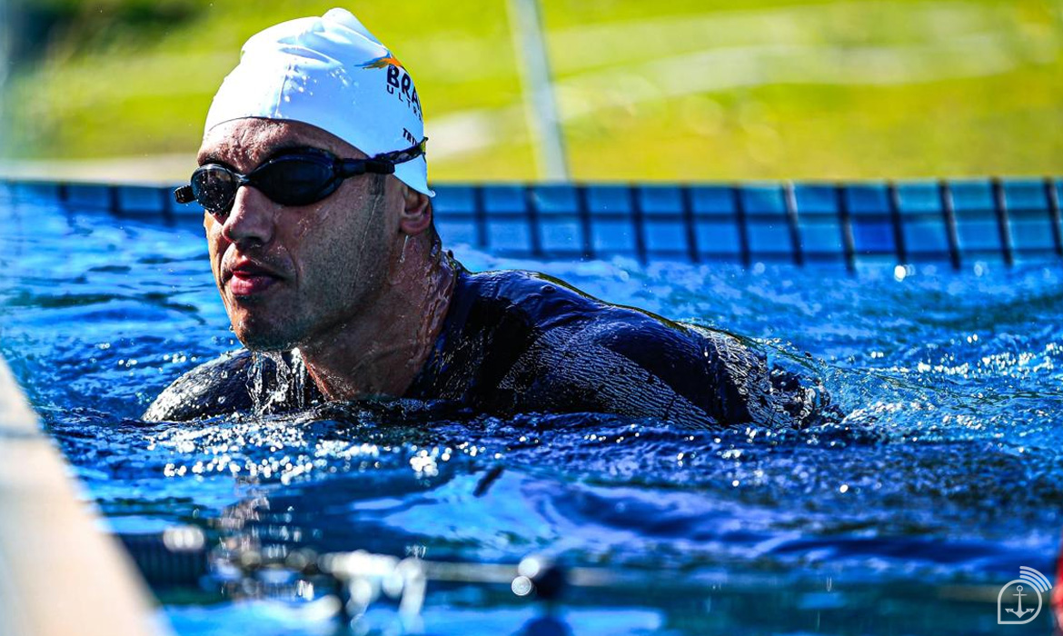 Atleta nadando em piscina, vestindo touca branca.