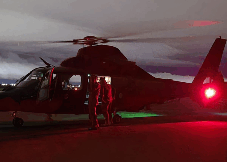 Helicóptero pousado à noite com luzes acesas.