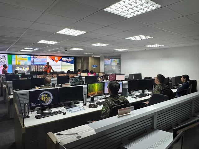 Pessoas trabalham em sala de operações com computadores.