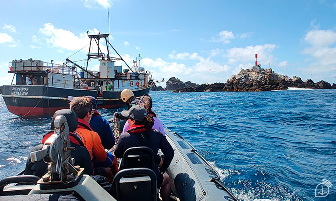 Lancha e barco próximos a farol no mar azul.