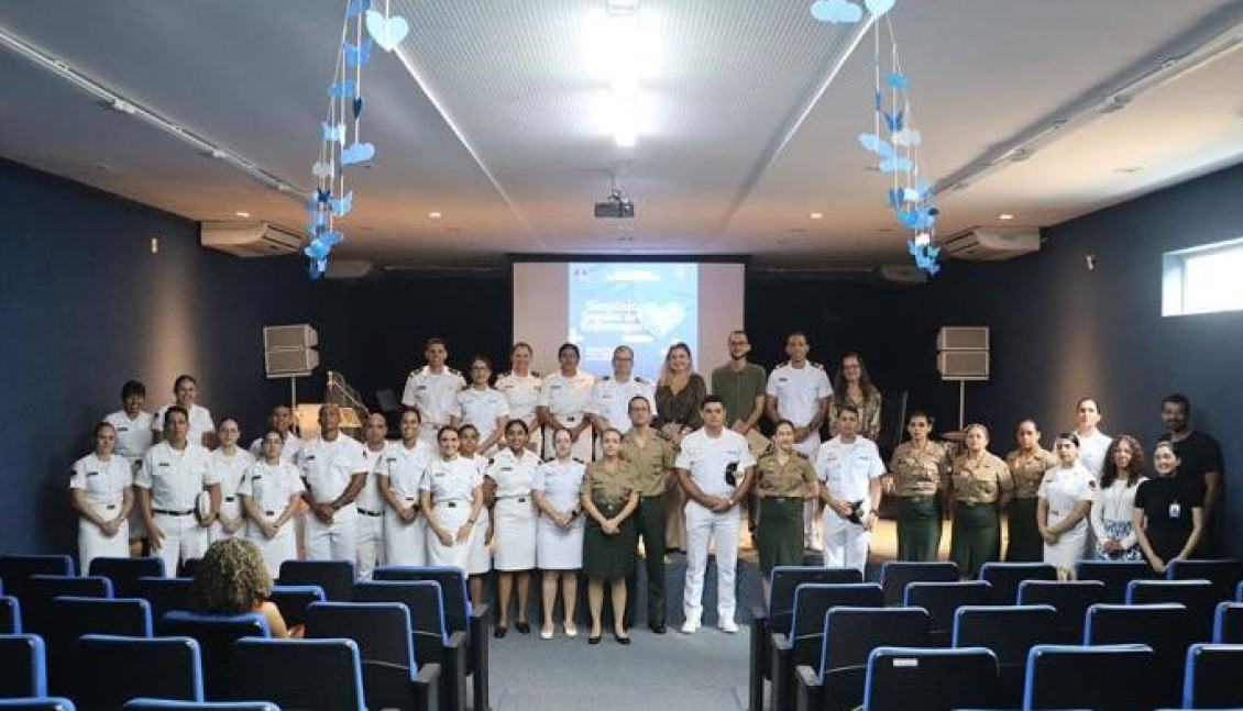 Pessoas em uniformes em auditório com tela ao fundo.