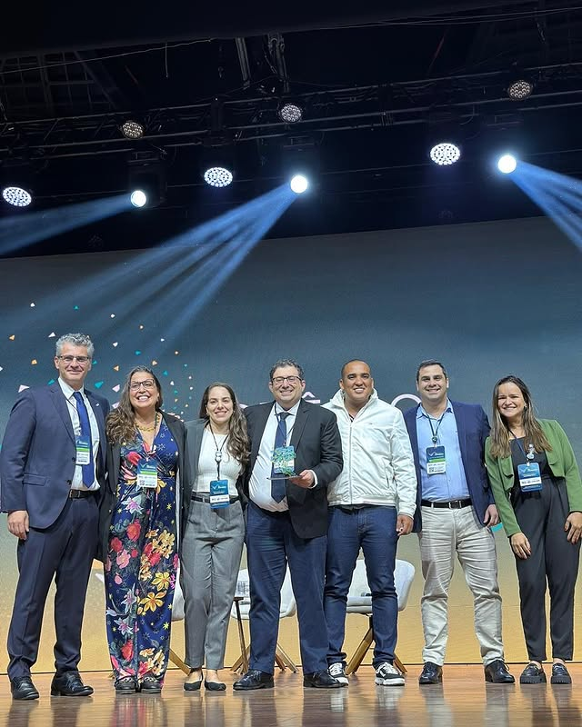 Grupo de pessoas sorrindo em um palco iluminado.