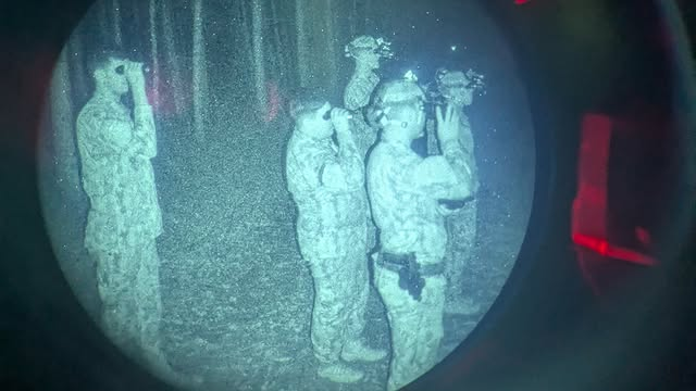 Soldados usando visão noturna em floresta escura.