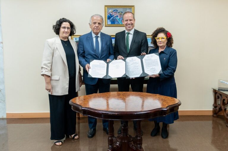 Quatro pessoas segurando documentos assinados na mesa.