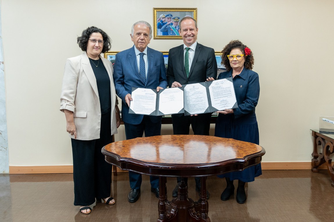 Quatro pessoas segurando documentos assinados na mesa.