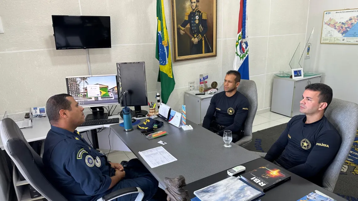 Reunião de policiais em escritório com bandeiras.
