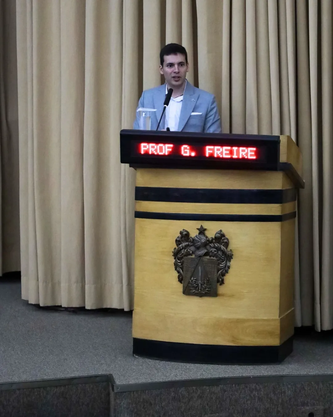 Homem apresentando palestra em auditório com púlpito.