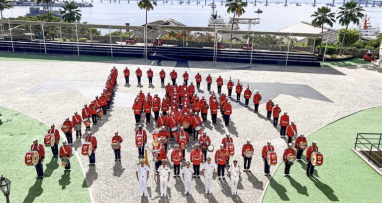 Banda militar se apresenta em praça à beira-mar.