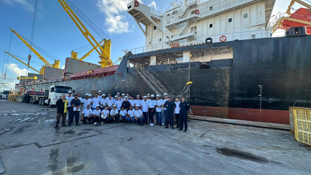 Equipe de trabalhadores em frente a navio cargueiro.