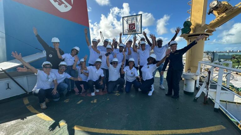 Grupo de pessoas sorrindo em navio com capacetes.