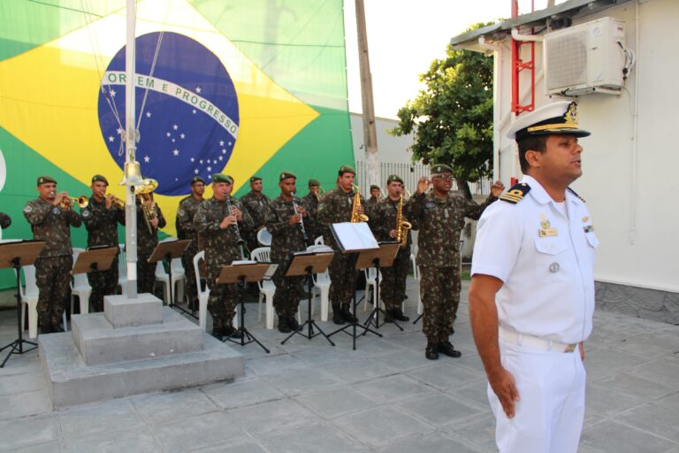 Banda militar toca, bandeira do Brasil ao fundo.