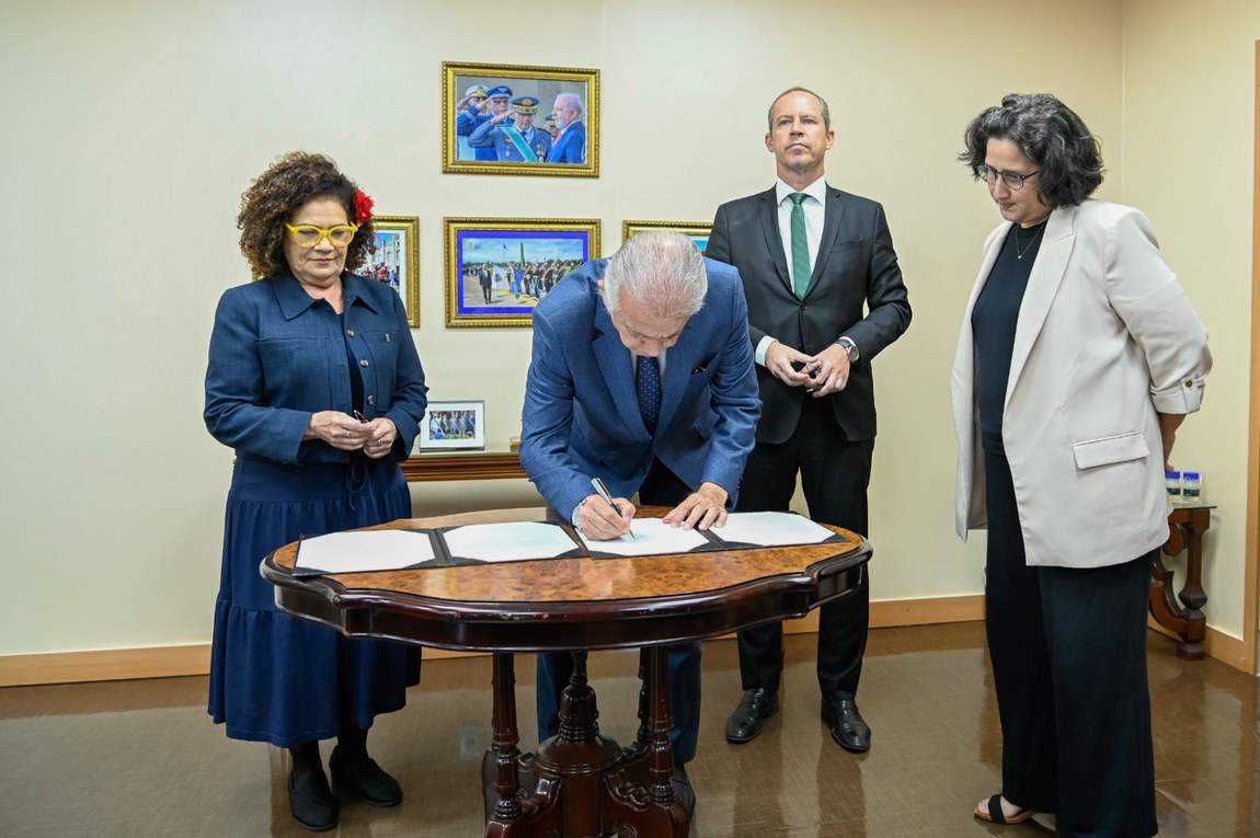 Autoridade assinando documento em cerimônia oficial.