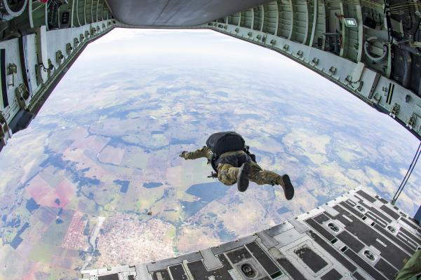 Paraquedista salta de avião militar em voo.