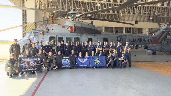 Equipe militar posando em frente a helicóptero naval.