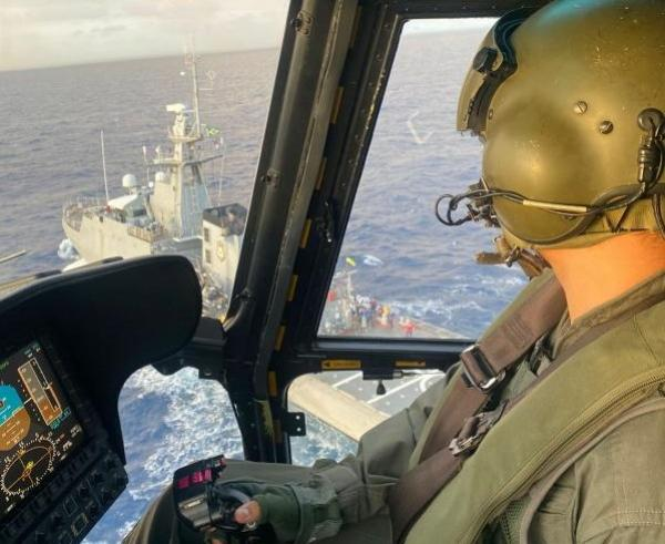 Piloto de helicóptero sobrevoa navio no oceano.