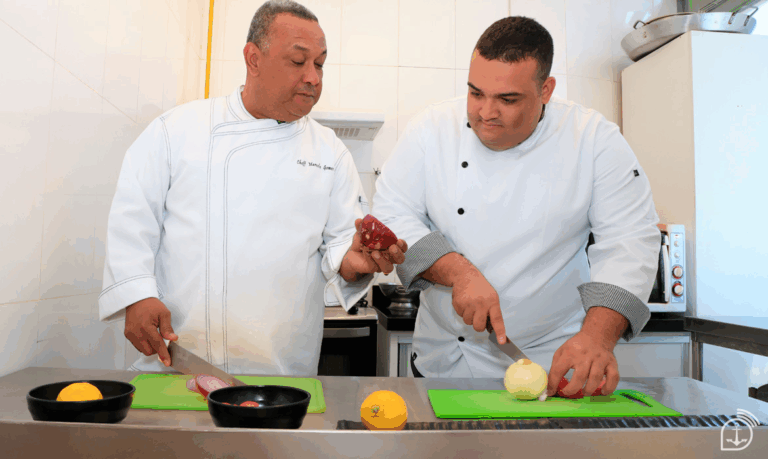 Dois chefs cortando legumes em cozinha profissional.