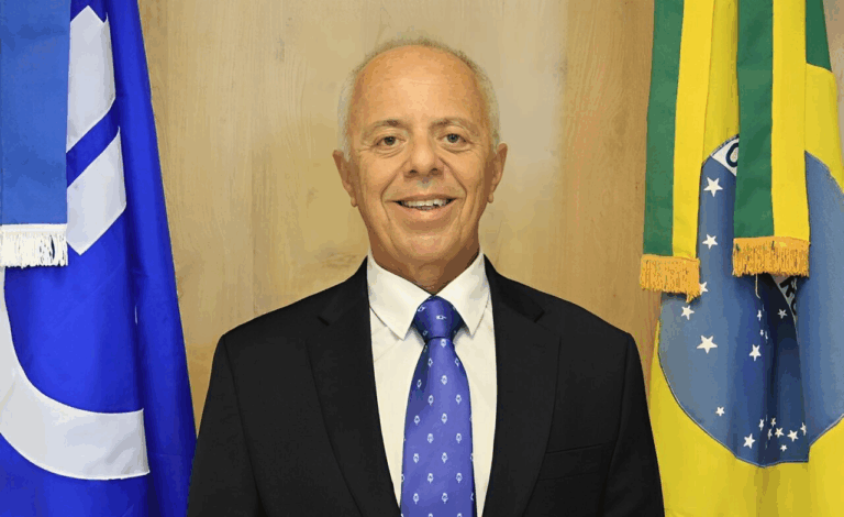 Homem seixas em terno ao lado de bandeiras do Brasil.
