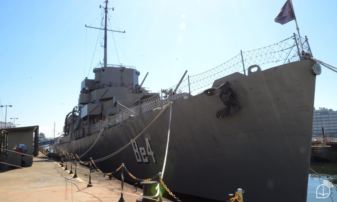 Navio de guerra atracado no porto sob sol forte.