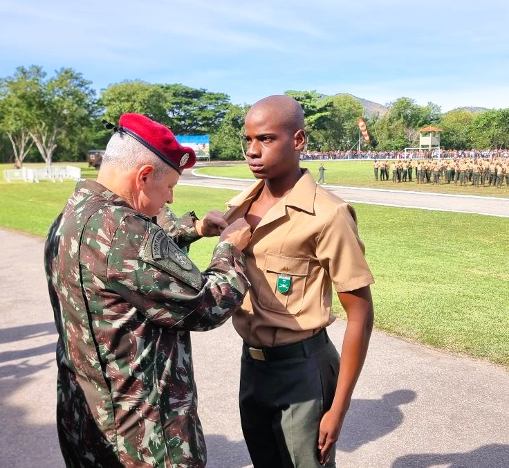 Soldado recebe medalha em cerimônia militar ao ar livre.