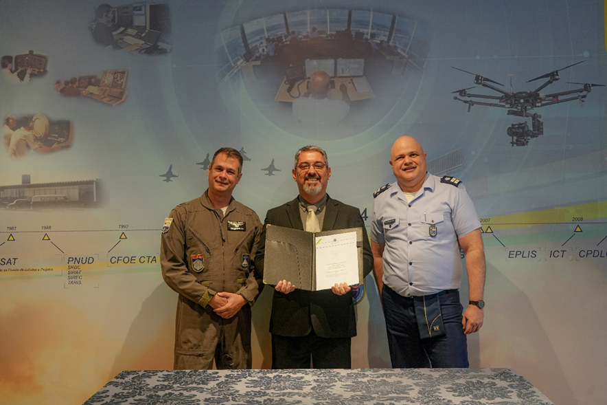 Três homens fardados posando com certificado.