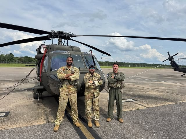 Três soldados em frente a um helicóptero militar.