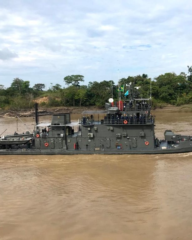 Navio militar navegando em rio cercado por floresta.