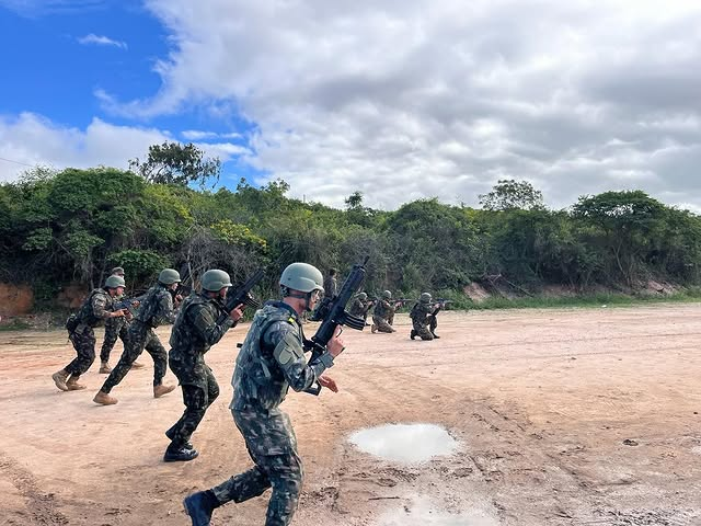 Soldados treinando em área aberta com armamento.