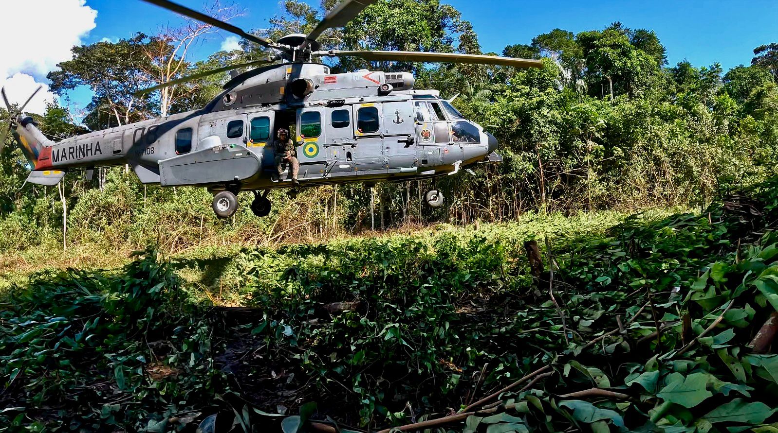 Helicóptero da Marinha voando sobre floresta densa.