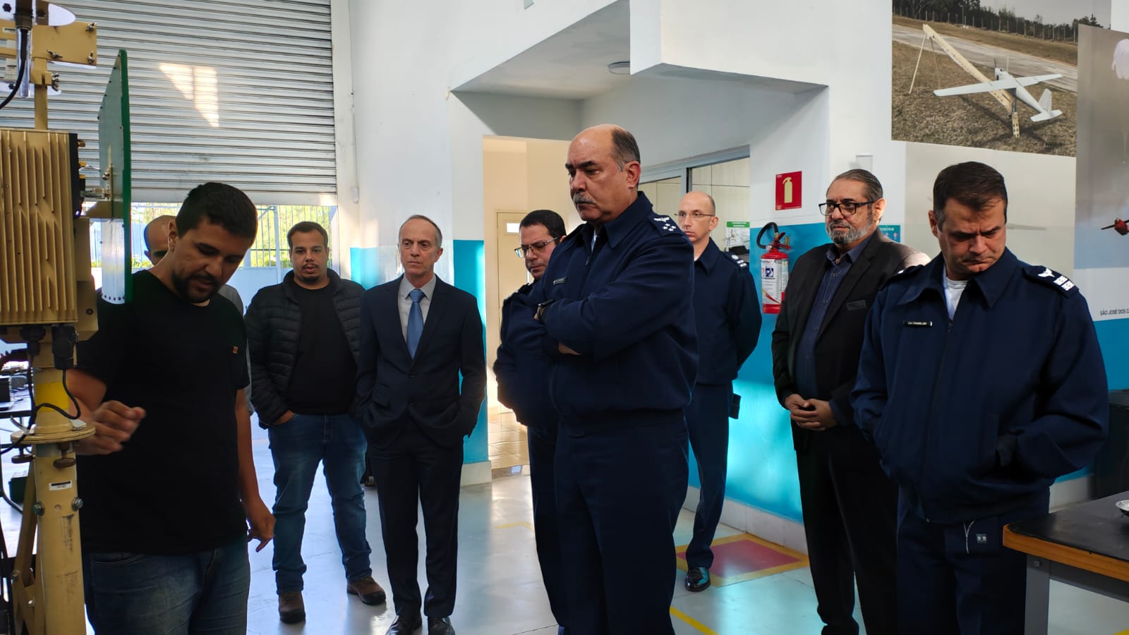 Pessoas em oficina com uniforme militar observando equipamento.