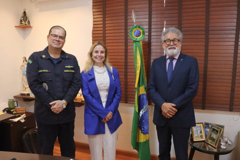 Três pessoas ao lado de bandeira do Brasil em escritório.
