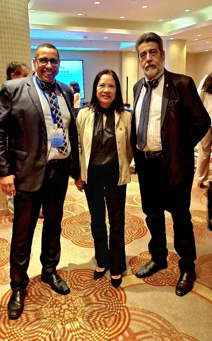 Três pessoas em evento formal, sorrindo para a câmera.