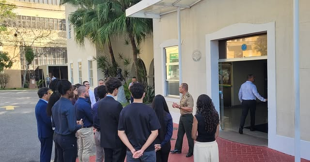Pessoas reunidas em frente a prédio, conversa formal.