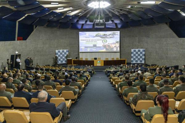 Conferência militar em auditório grande, pessoas uniformizadas.