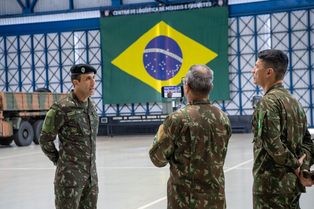 Militares do Exército em frente à bandeira brasileira.
