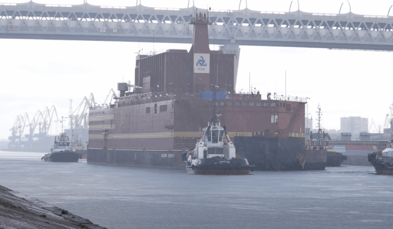 Rebocador transportando plataforma nuclear sob ponte.
