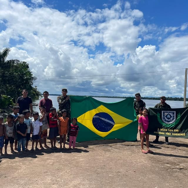 Crianças e militares com bandeira brasileira à beira d'água.